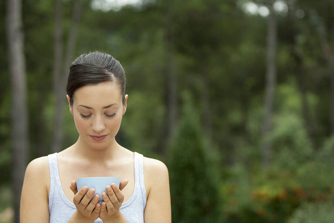 Young woman holding bowl in cupped hands with eyes closed