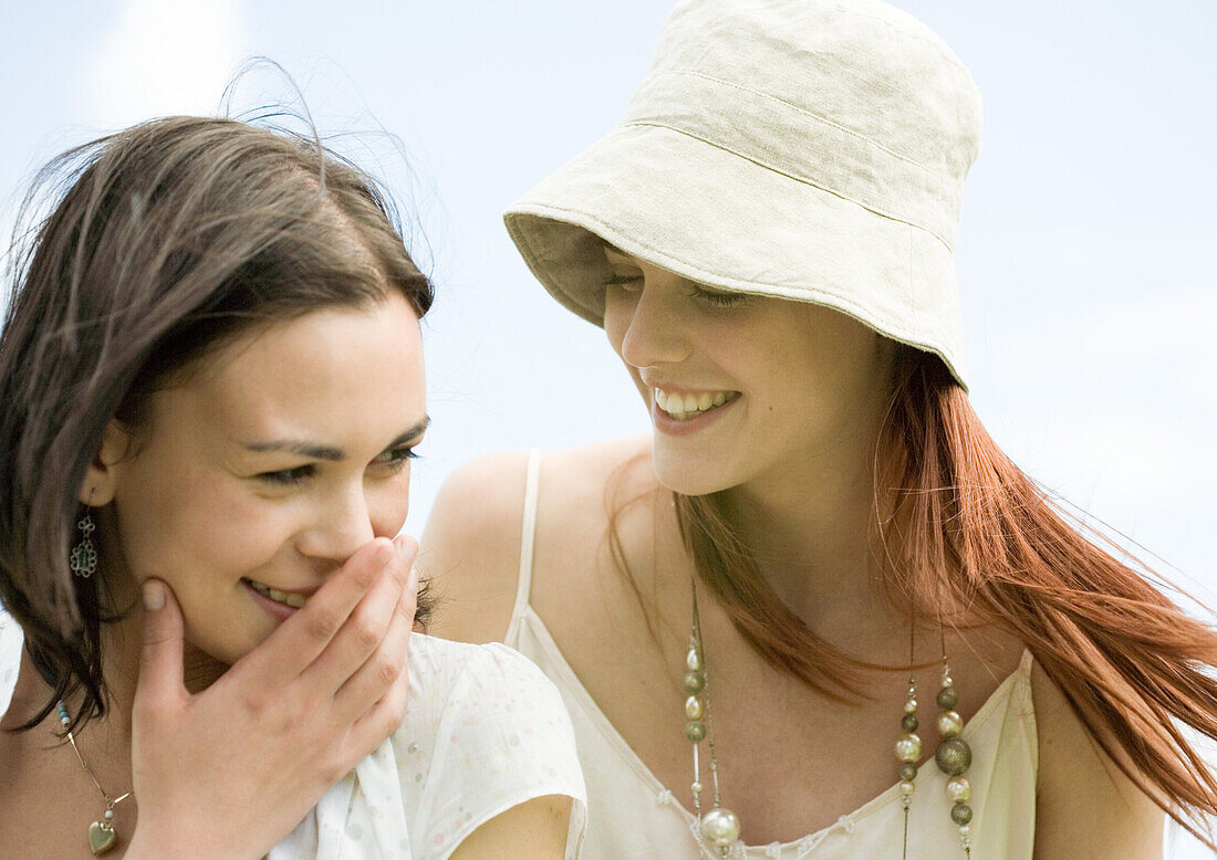 Two young women smiling, one covering mouth