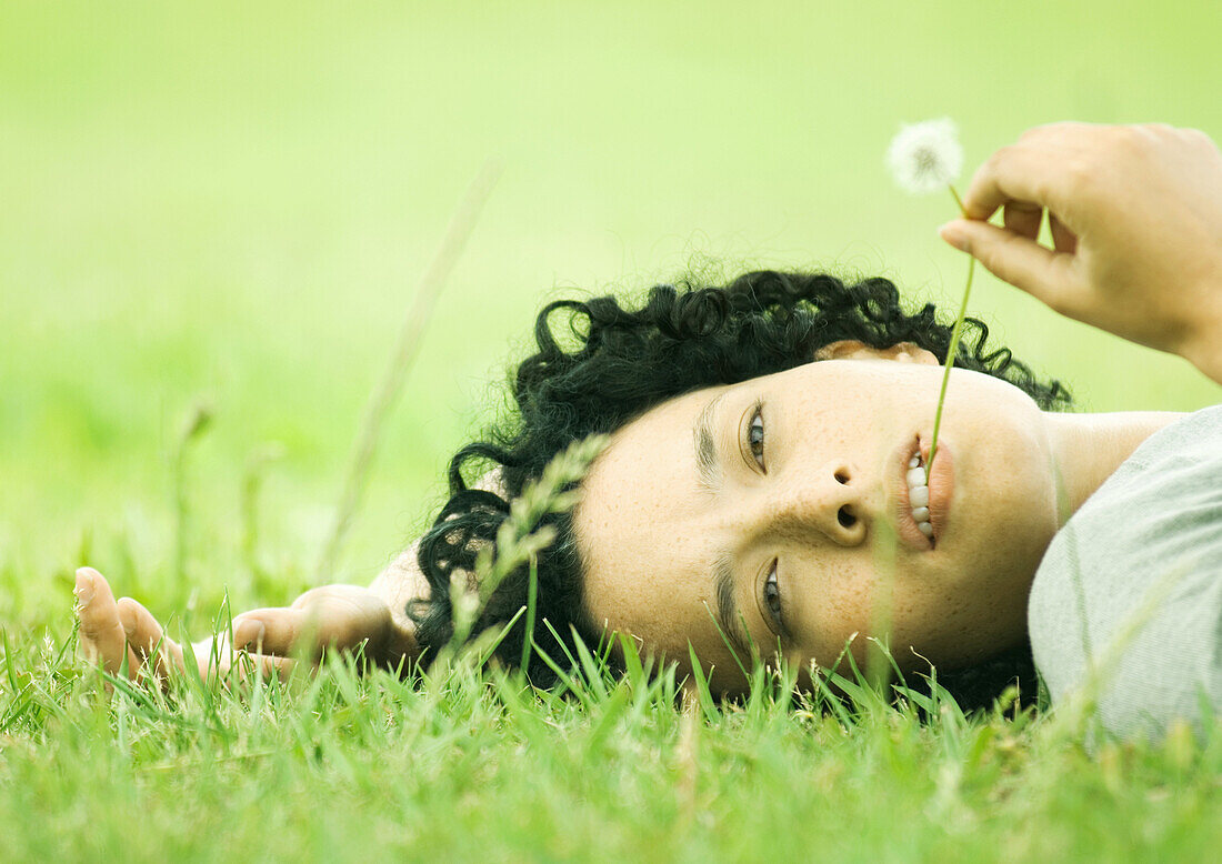 Woman lying on grass with dandelion in mouth