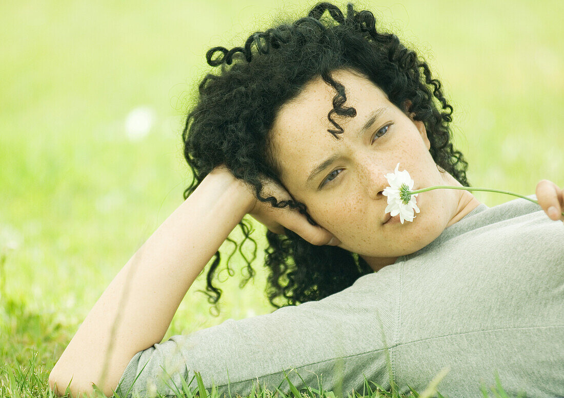 Woman lying on ground and holding daisy to nose