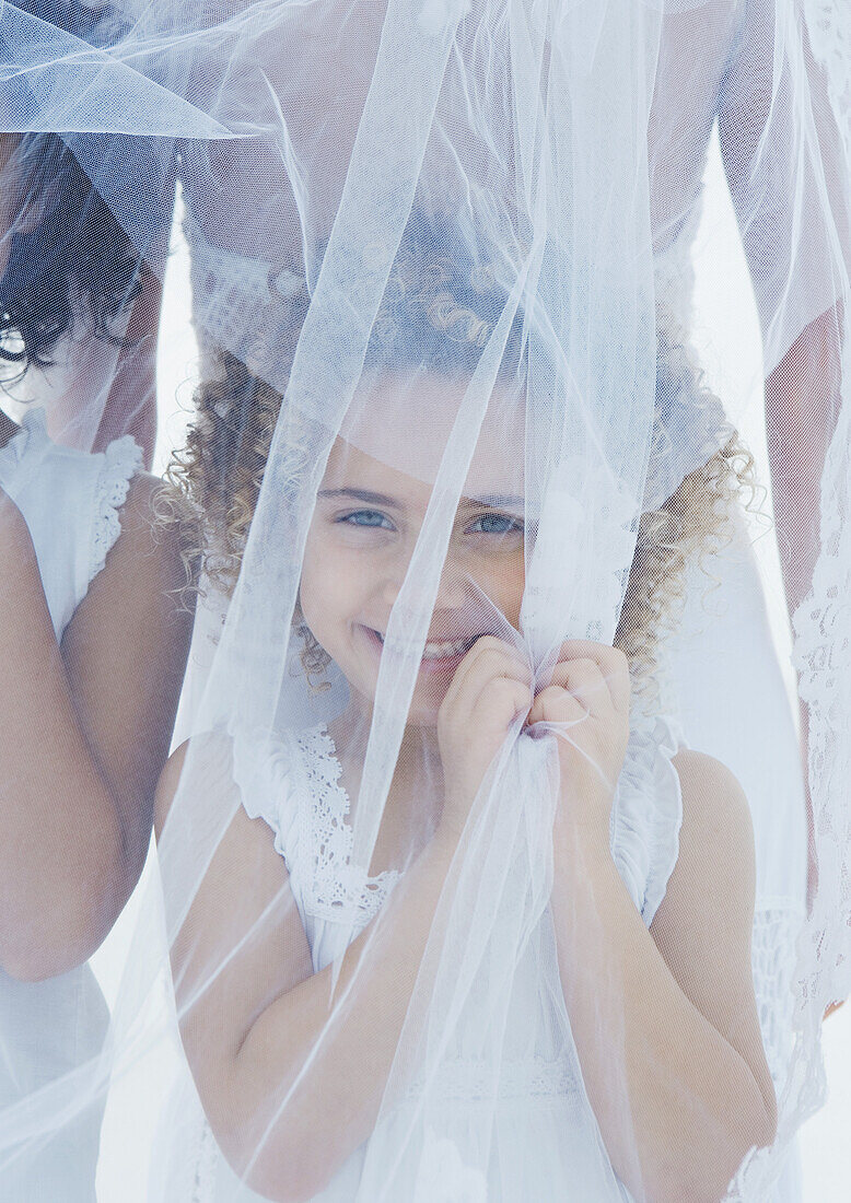 Little girl standing underneath bride's veil
