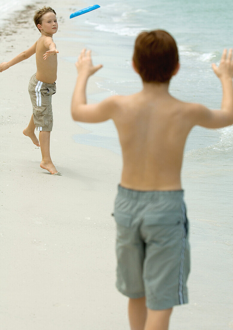 Boys throwing frisbee on beach