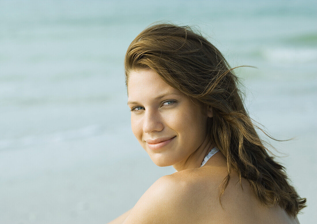 Young woman on beach, smiling over shoulder at camera