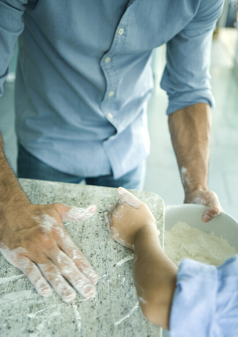 Girl and father wiping flour on counter into mixing bowl, cropped view