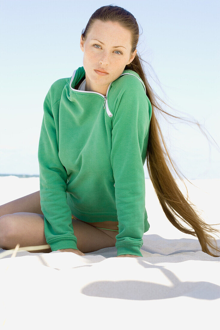 Young woman sitting on beach, looking at camera