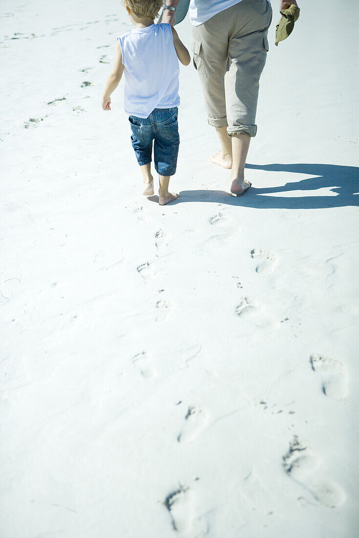 Child and adult walking on sand, low section