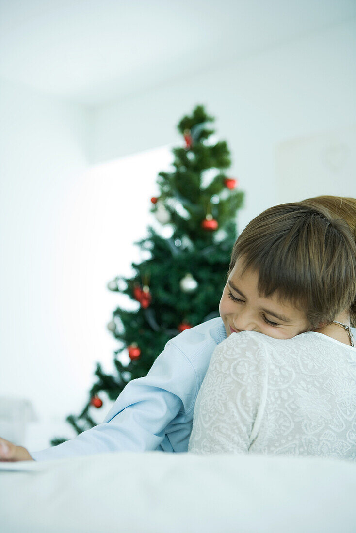 Mother sitting on sofa, holding boy in arms, Christmas tree in background, boy smiling