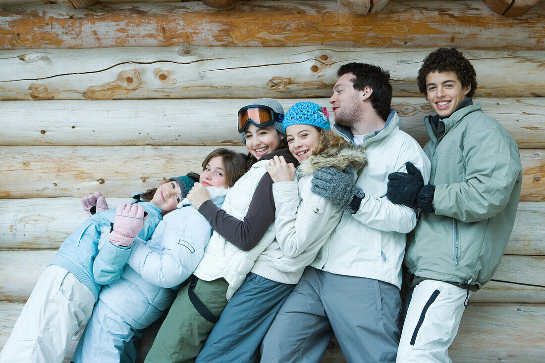 Group in winter clothes falling back onto each other, three quarter length, in front of log wall, portrait