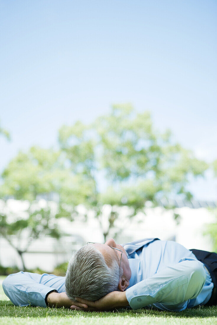 Mature businessman lying on ground outdoors, hands behind head