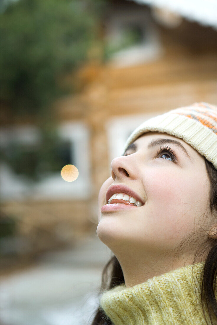 Teenage girl looking up, close-up, chalet in background