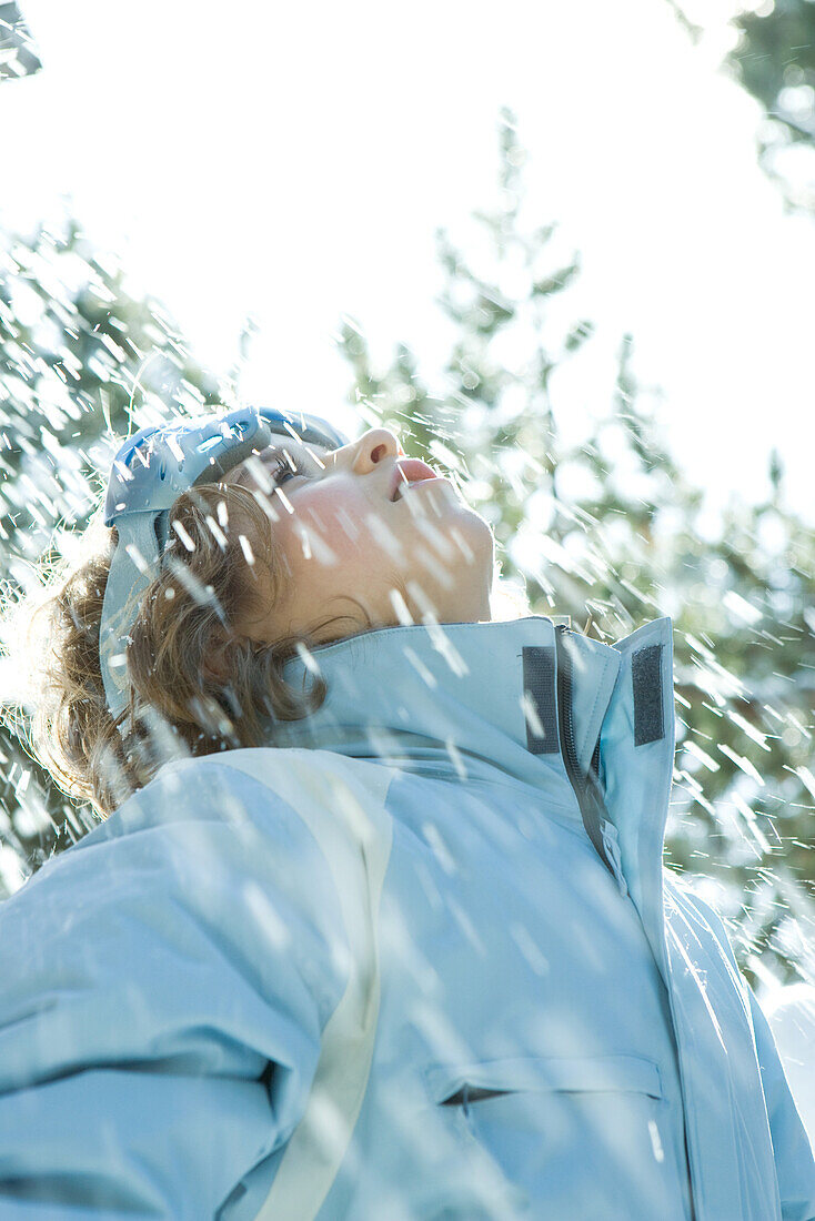 Girl standing in falling snow, head back, looking up