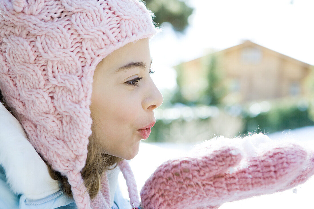 Preteen girl blowing handful of snow in mittens, side view