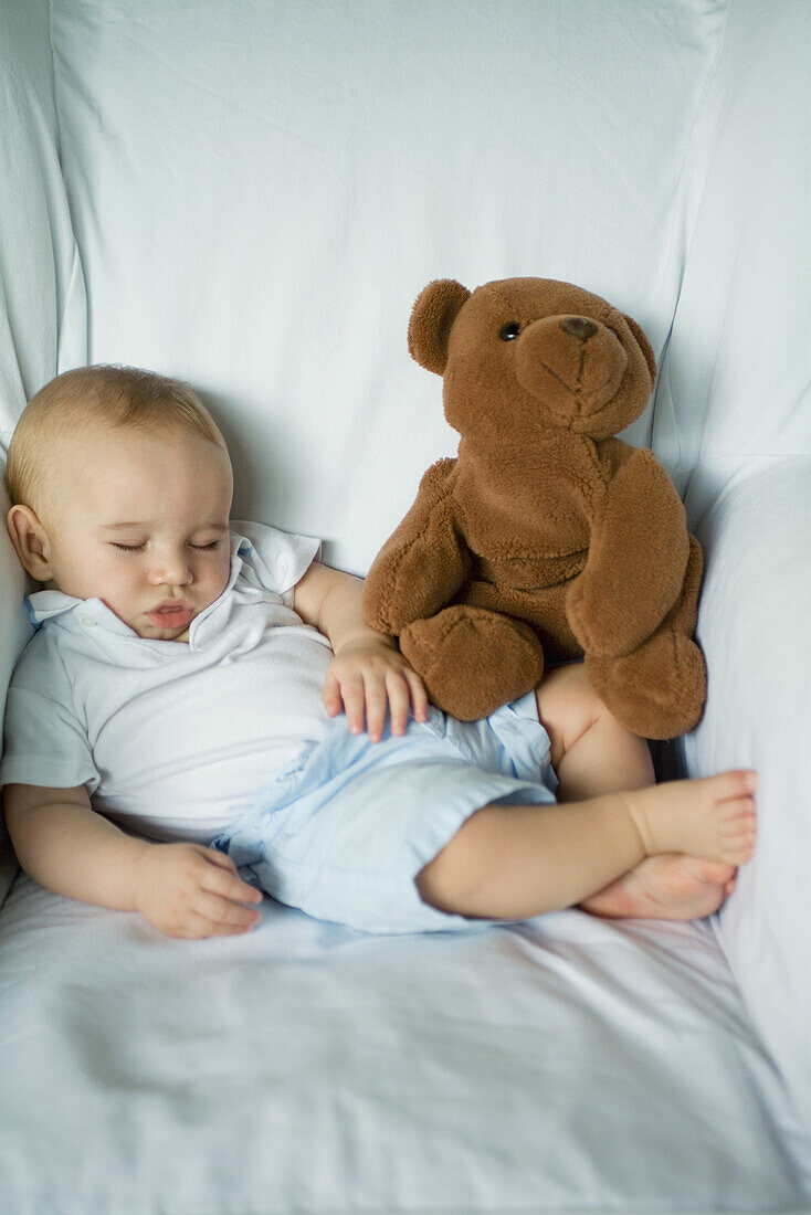 Baby sleeping in arm chair with teddy bear, portrait