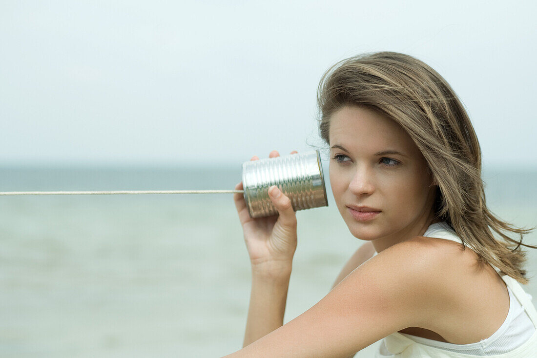 Teen girl holding tin can phone up to ear, looking away, portrait