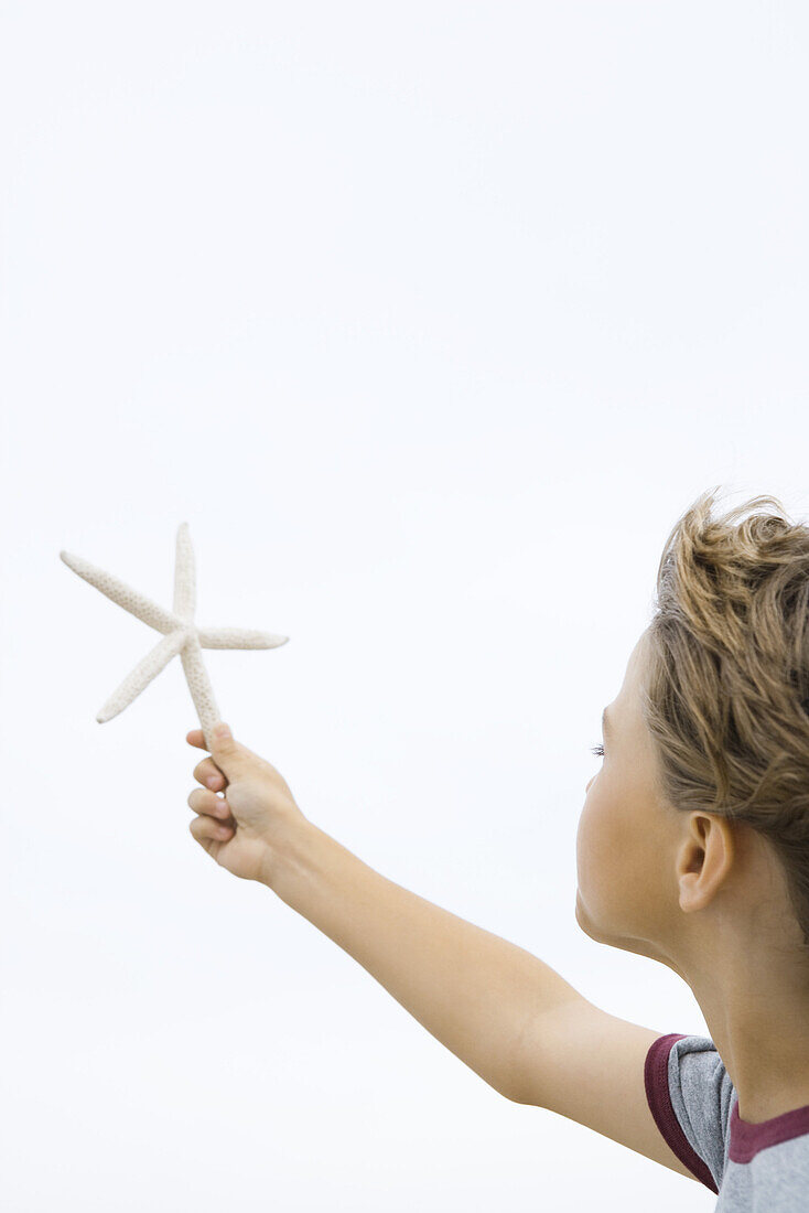 Boy holding up starfish, cropped side view