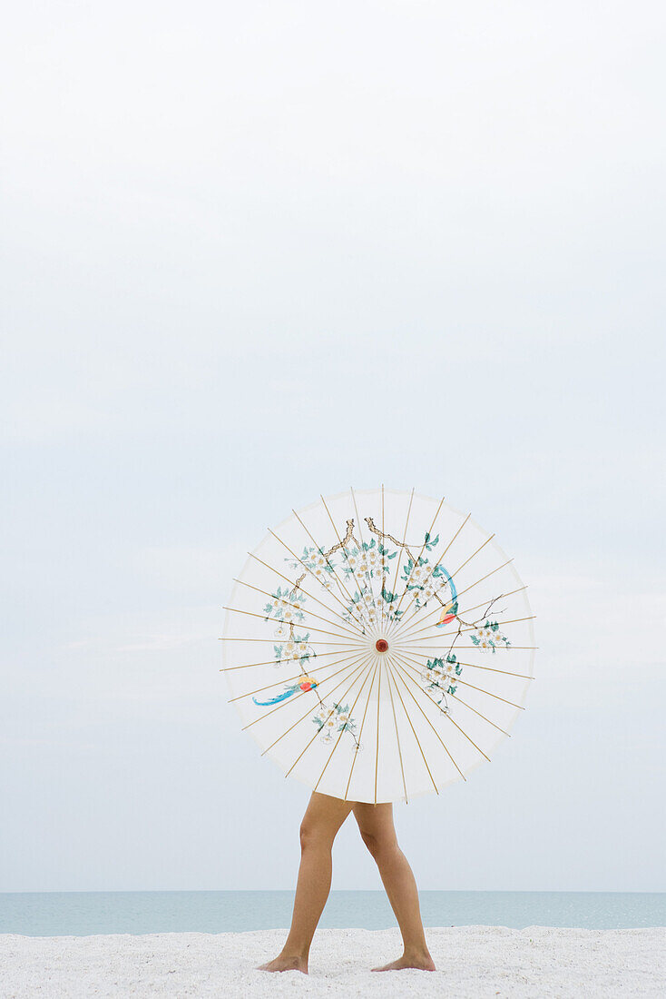 Woman behind parasol walking on beach, full length