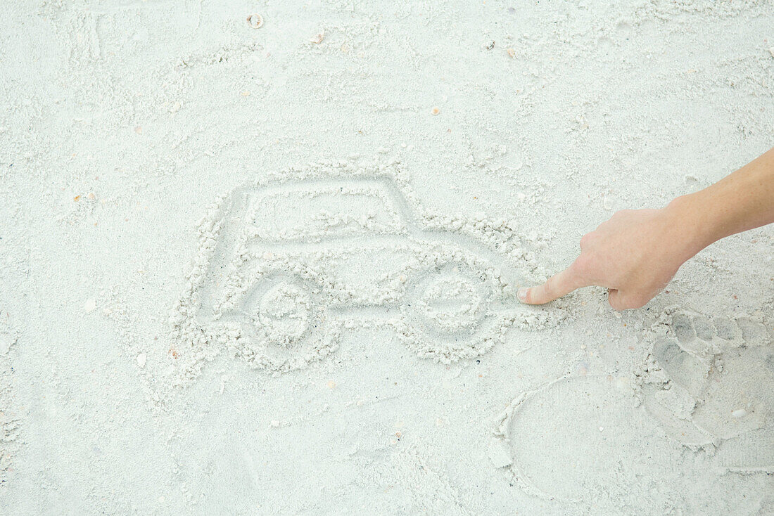 Teenage boy drawing car in sand, cropped view
