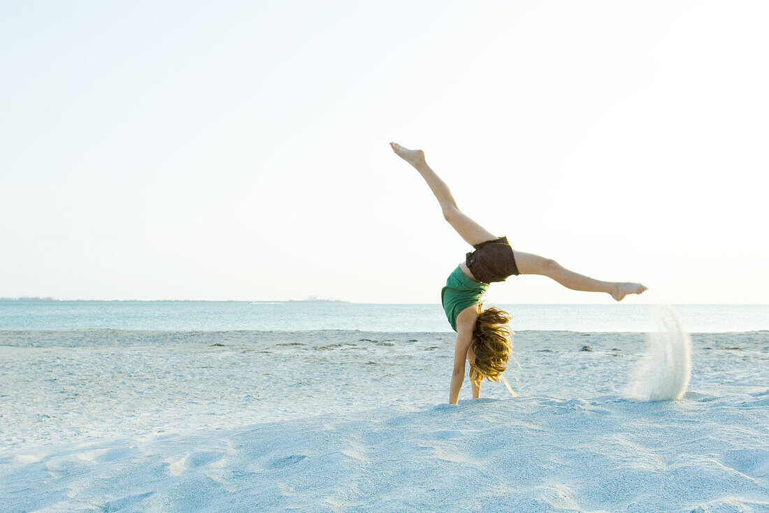 Little girl doing handstand at the beach, side view
