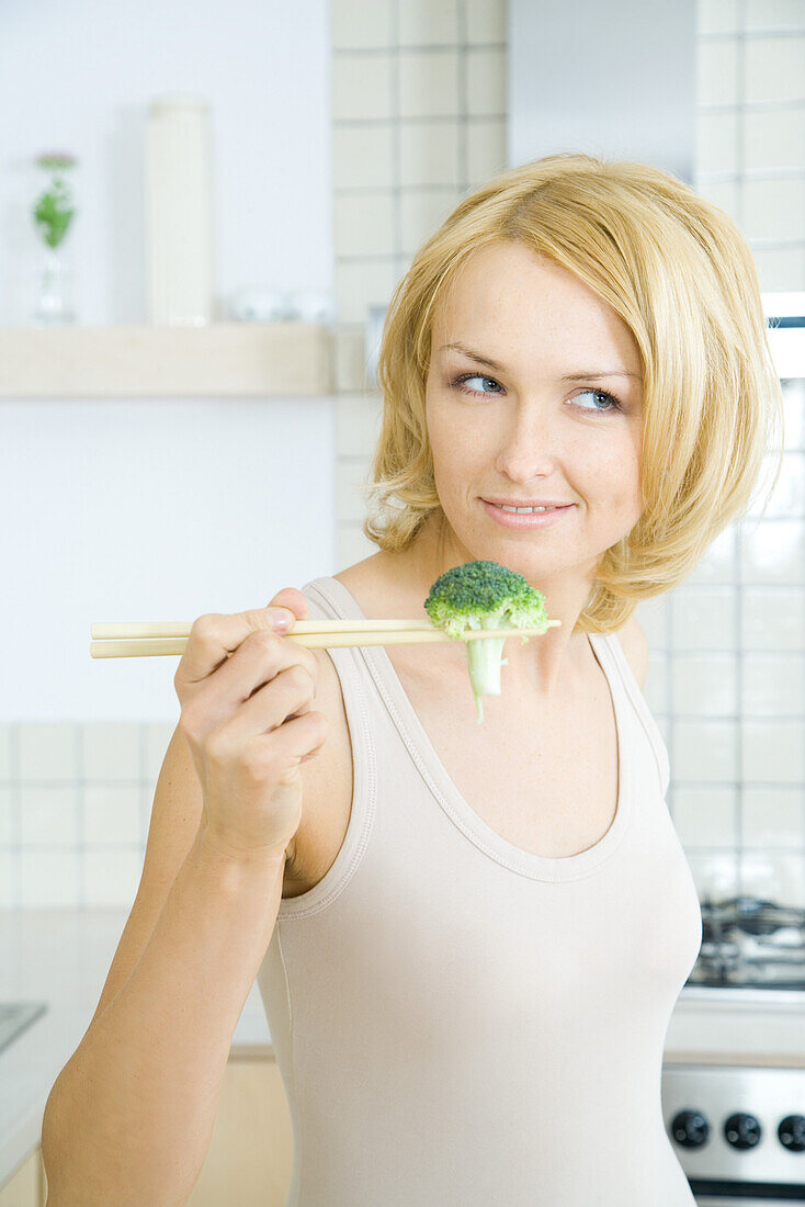 Blonde woman holding piece of broccoli with chopsticks