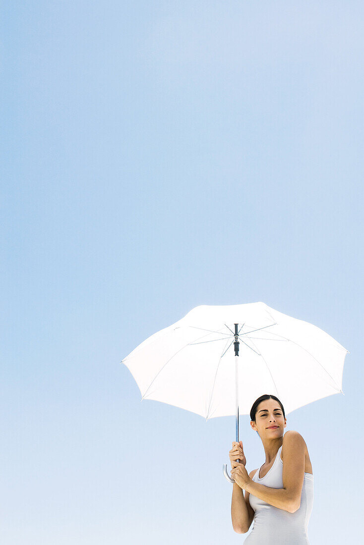 Woman standing under umbrella, smiling at camera, low angle view