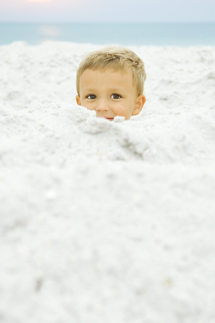 Boy's head emerging from sand, smiling at camera