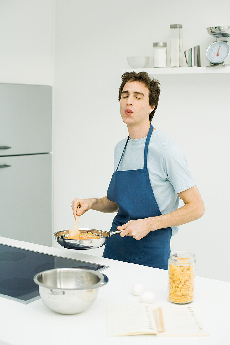Man standing at stove, cooking, eyes closed, whistling