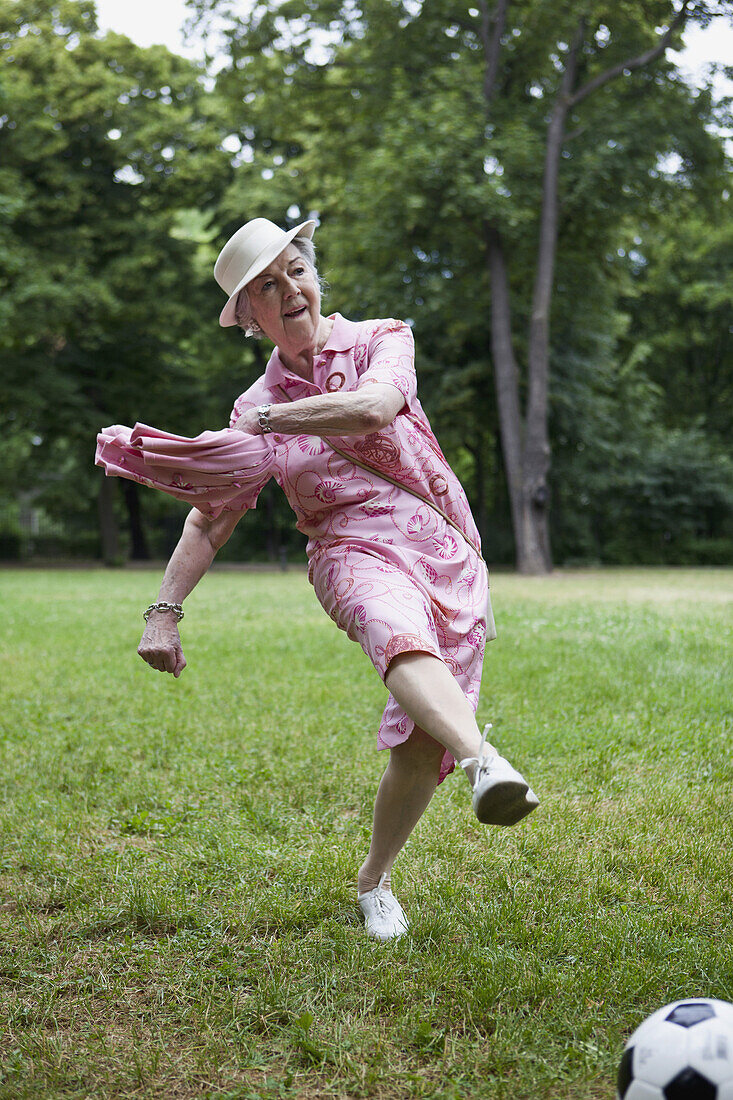 Senior woman kicks football n the park