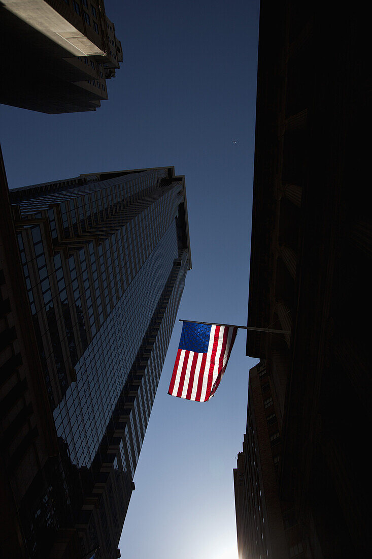 The American flag shown between skyscrapers with a backdrop of a clear blue sky