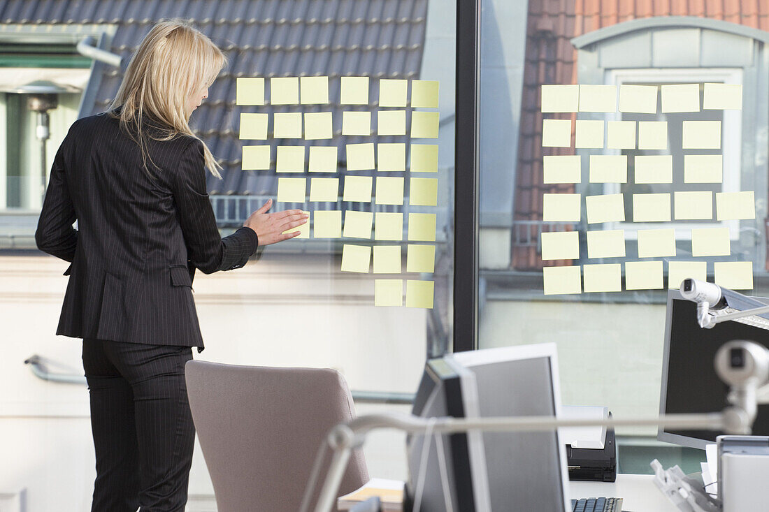 Businesswoman sticking many reminder notes to her office window