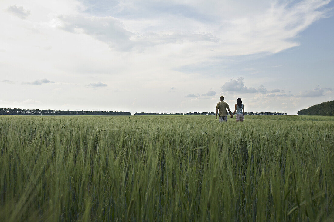 A man and woman walking hand in hand through a remote wheat field