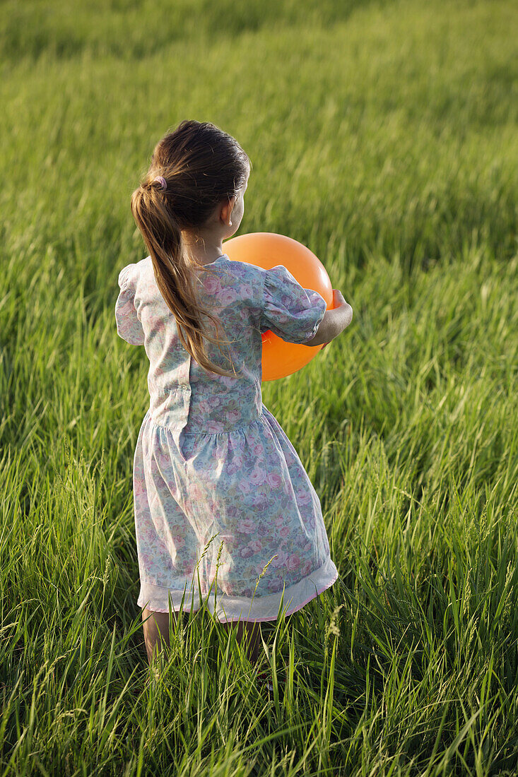 Rear view of a girl holding a balloon in a field