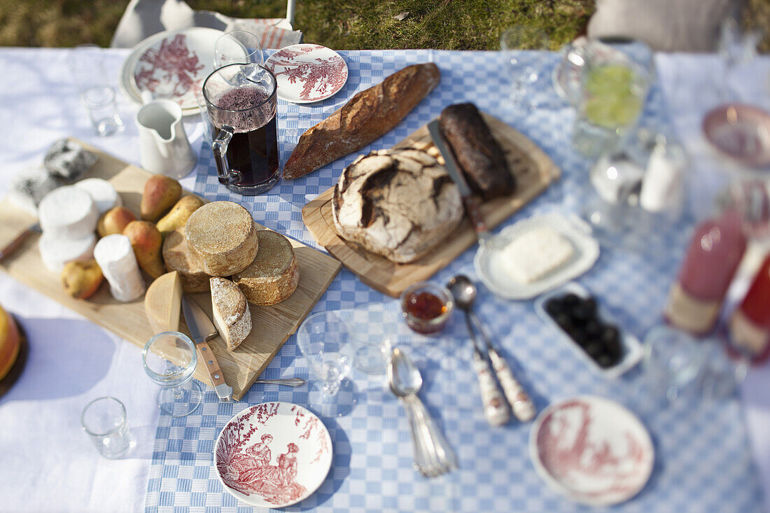 cheese wheels, bread and a lot of crockery on a dining table outside
