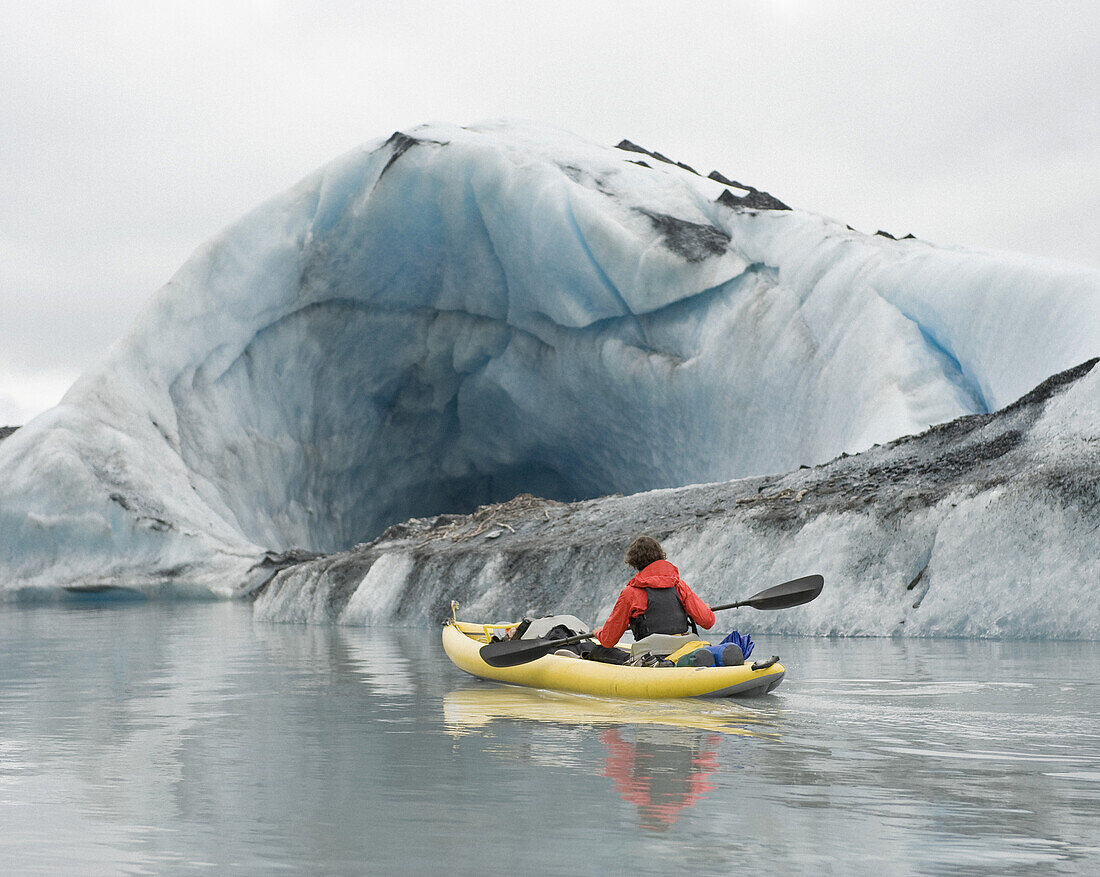 Kayaker paddling beside ice cave at Valdez Glacier, Alaska, USA