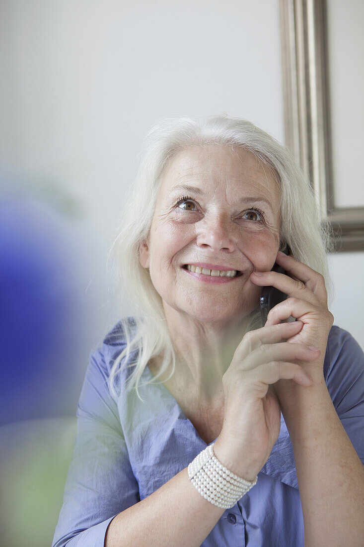 Happy senior woman answering mobile phone at home