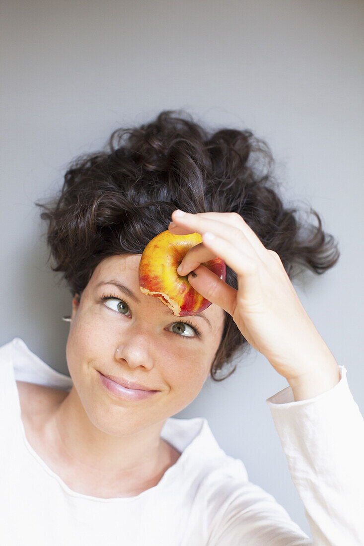 A woman holding apple on forehead over grey background