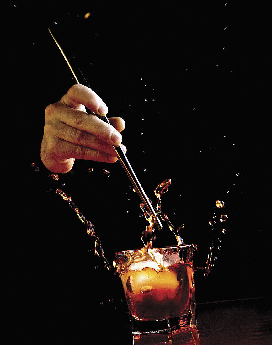 Hand dropping ice into whiskey over black background