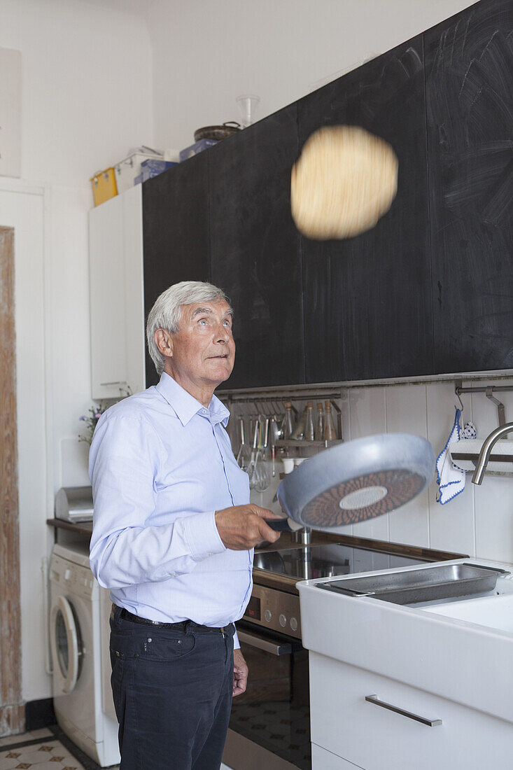 Senior man tossing pancake on frying pan in kitchen at home