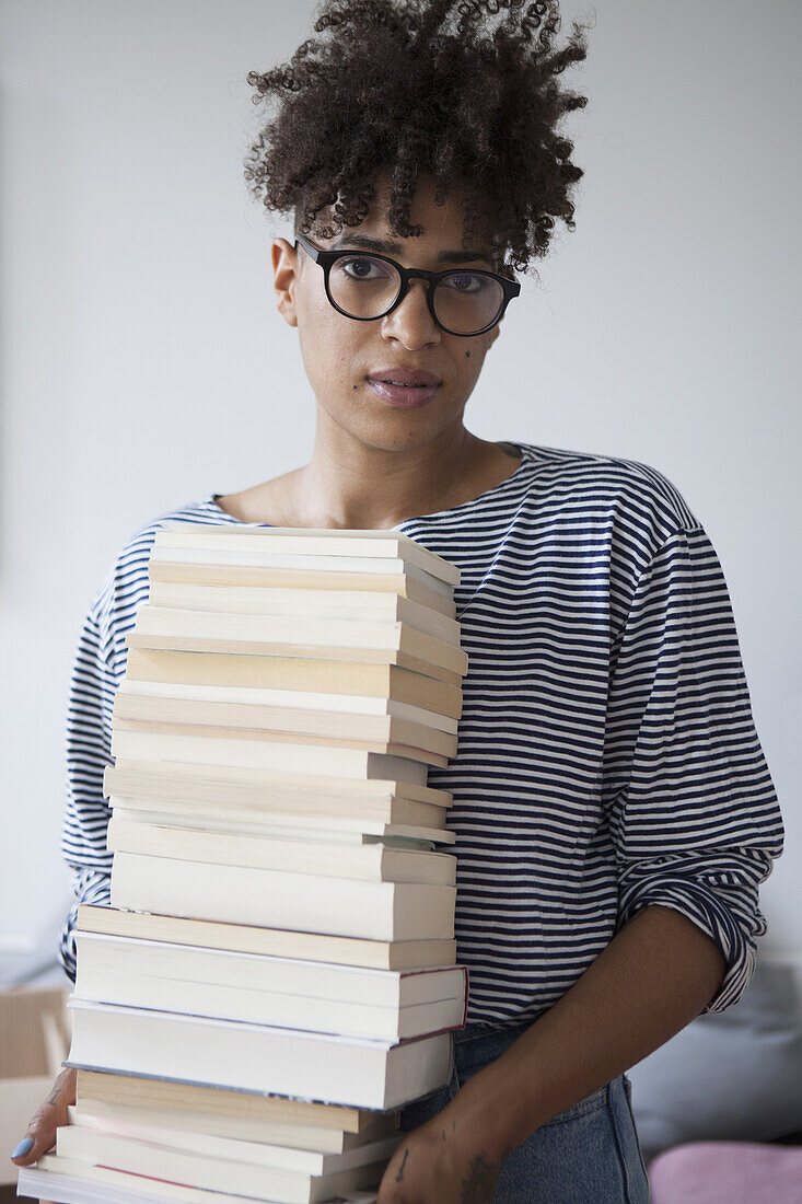 Portrait of confident young woman carrying stack of books at home