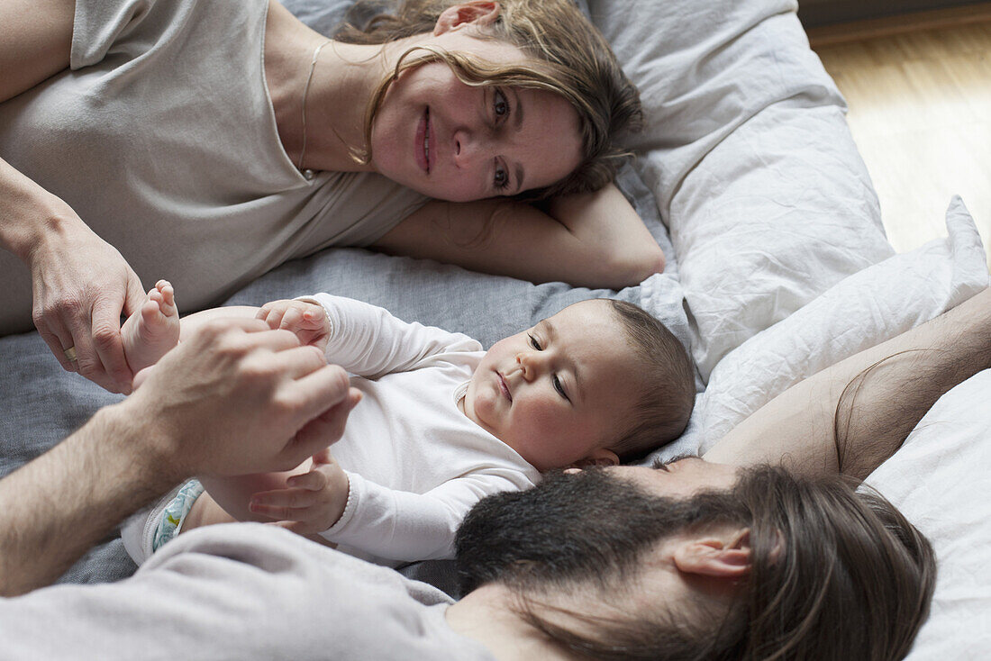 Affectionate parents looking at baby girl while relaxing on mattress