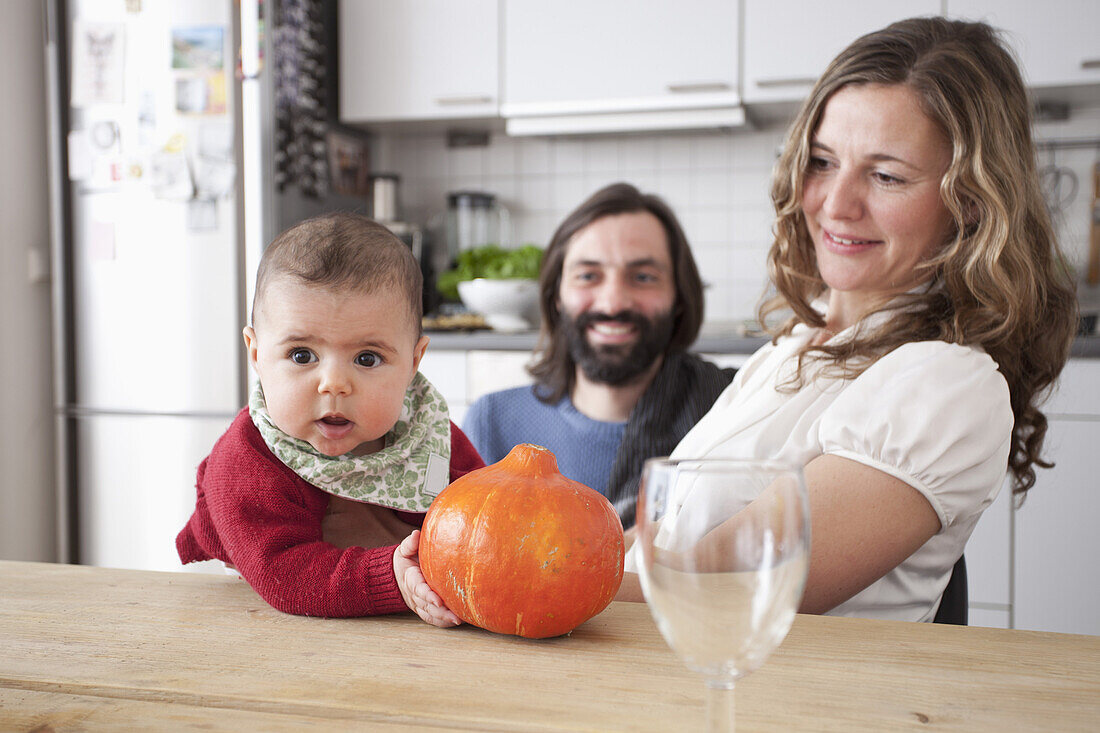 Parents with baby girl holding pumpkin at table in kitchen