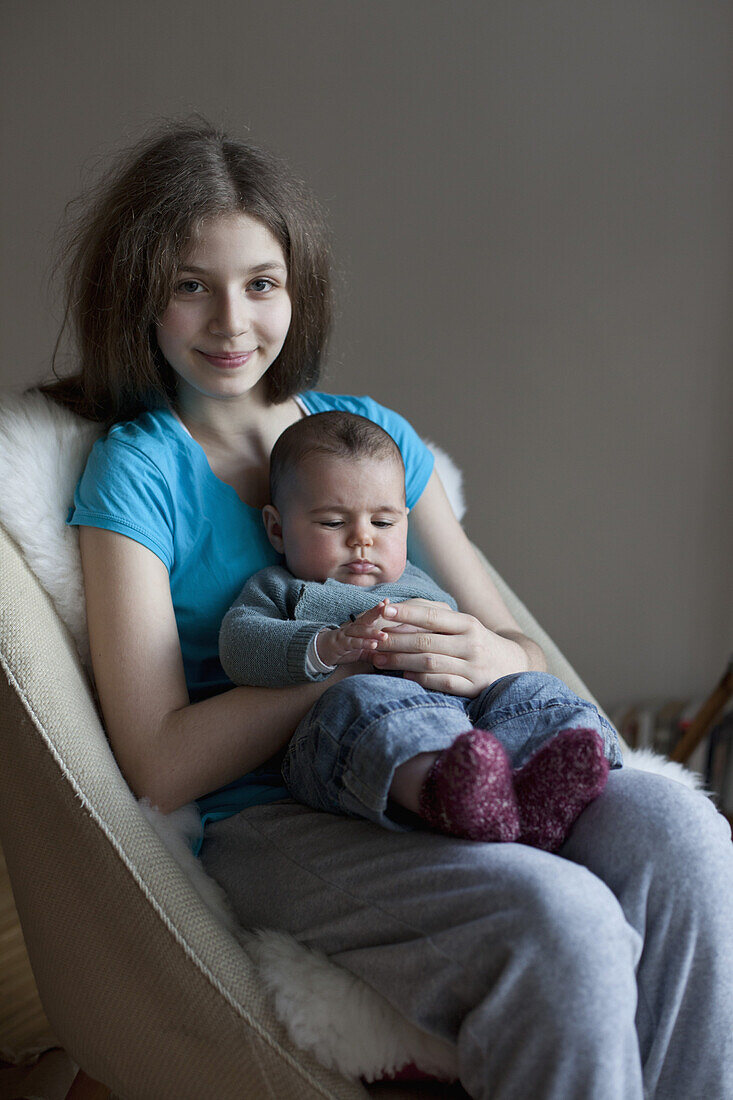 Portrait of smiling sister with baby girl on chair at home
