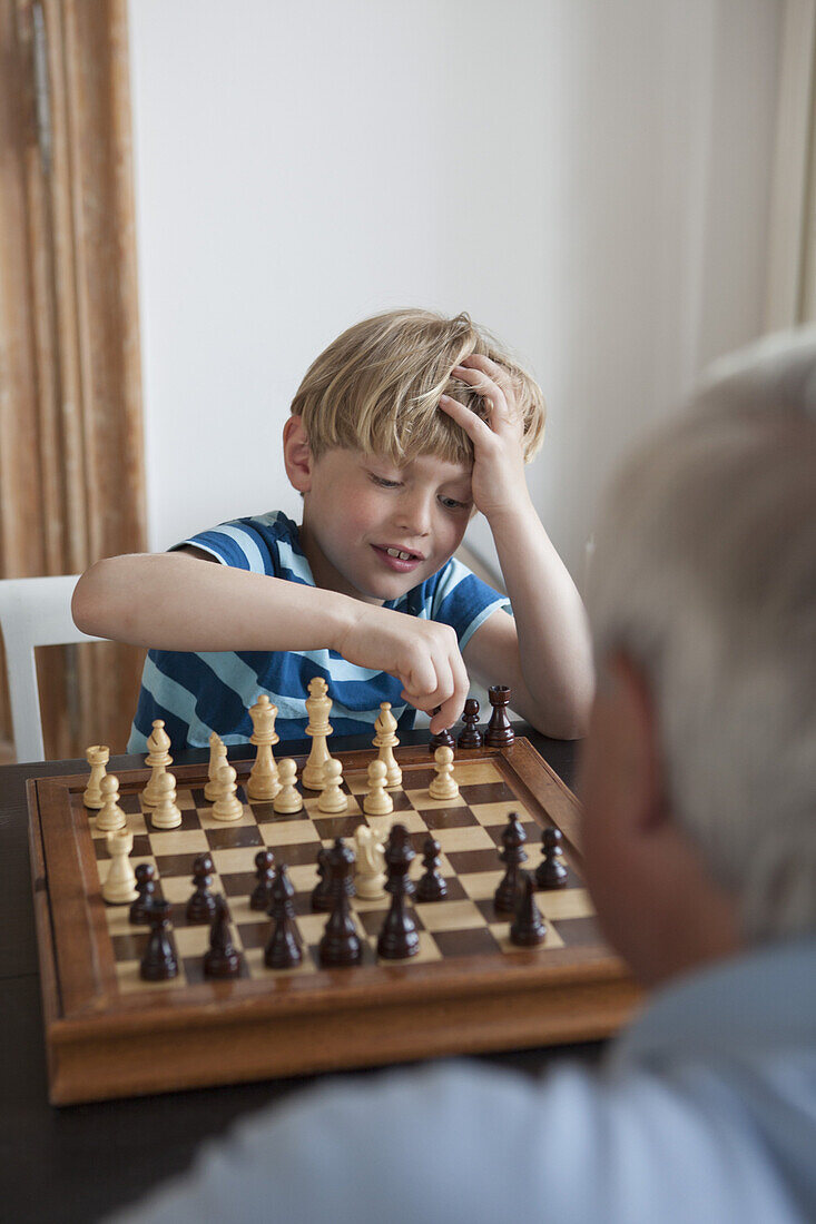 Little boy playing chess with grandfather at home