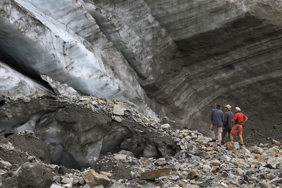Three men standing at the foot of a glacier