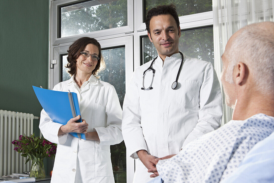 Two doctors next to a male patient in a hospital ward