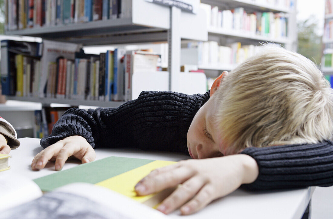 A boy taking a nap on a desk in a library