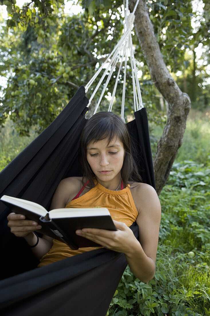 Young woman lying in hammock and reading