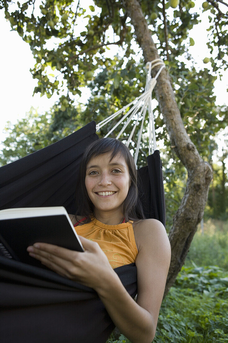 Young woman smiling and reading book in hammock