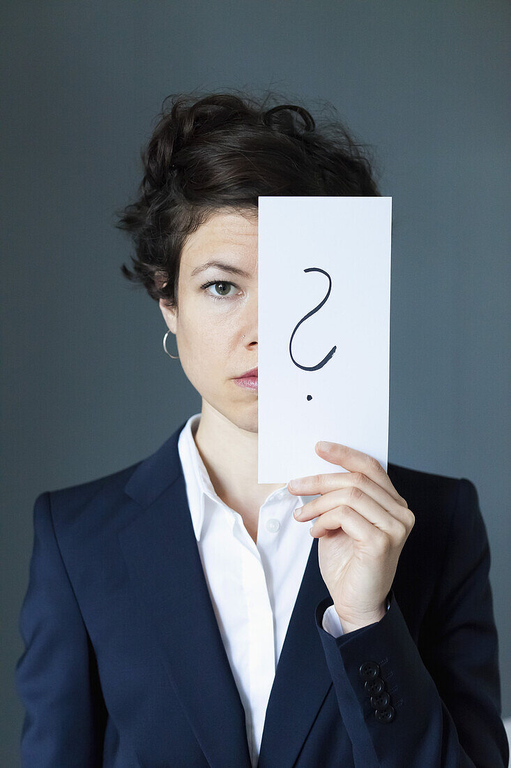Portrait of mid adult woman holding paper with question mark, close-up