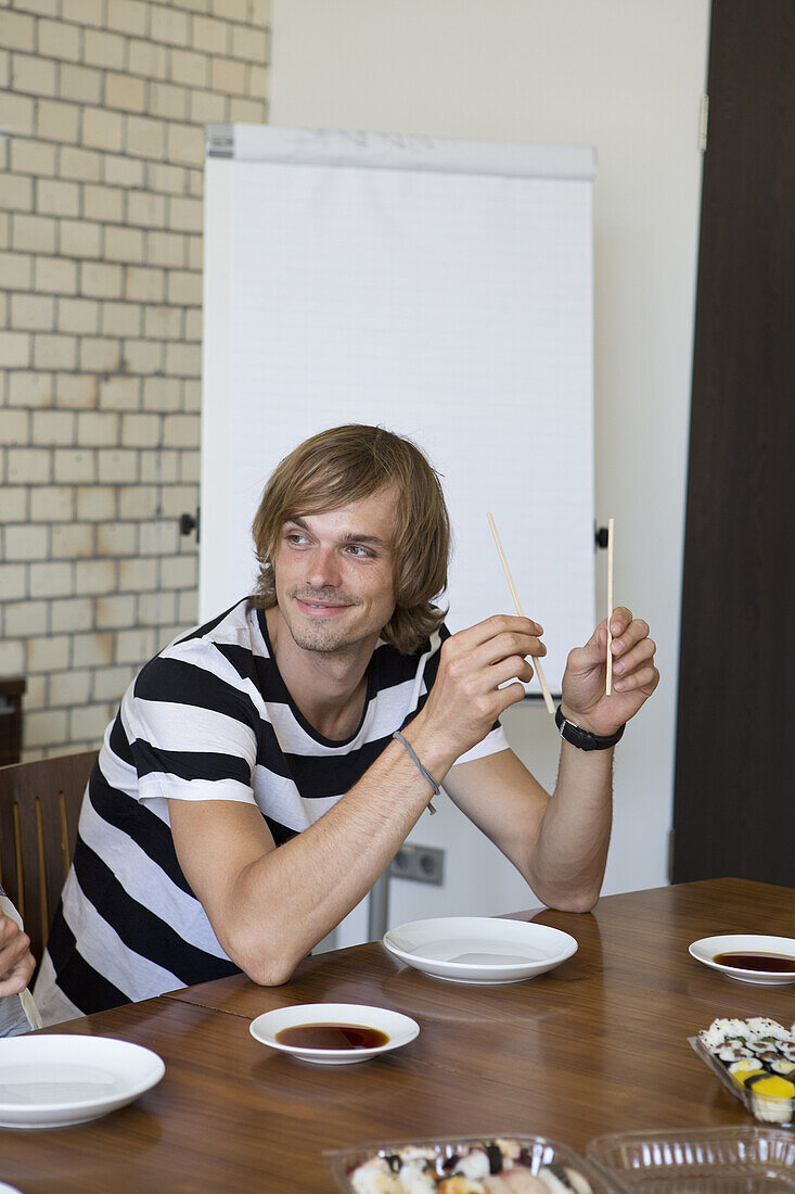 Man sitting at table holding chopsticks, smiling