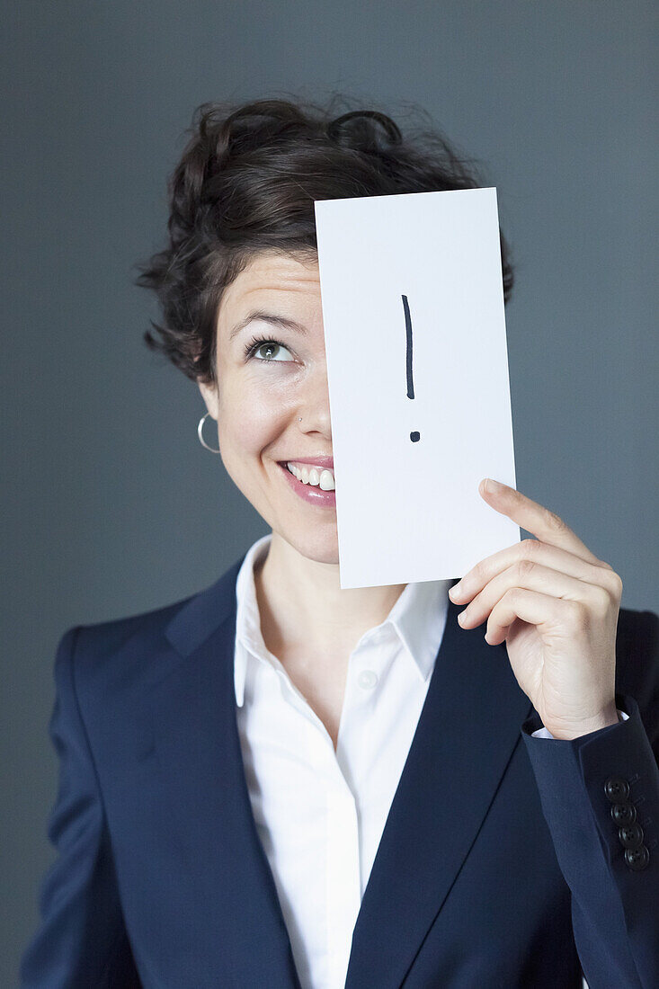 Mid adult woman holding paper with exclamation mark and smiling, close-up